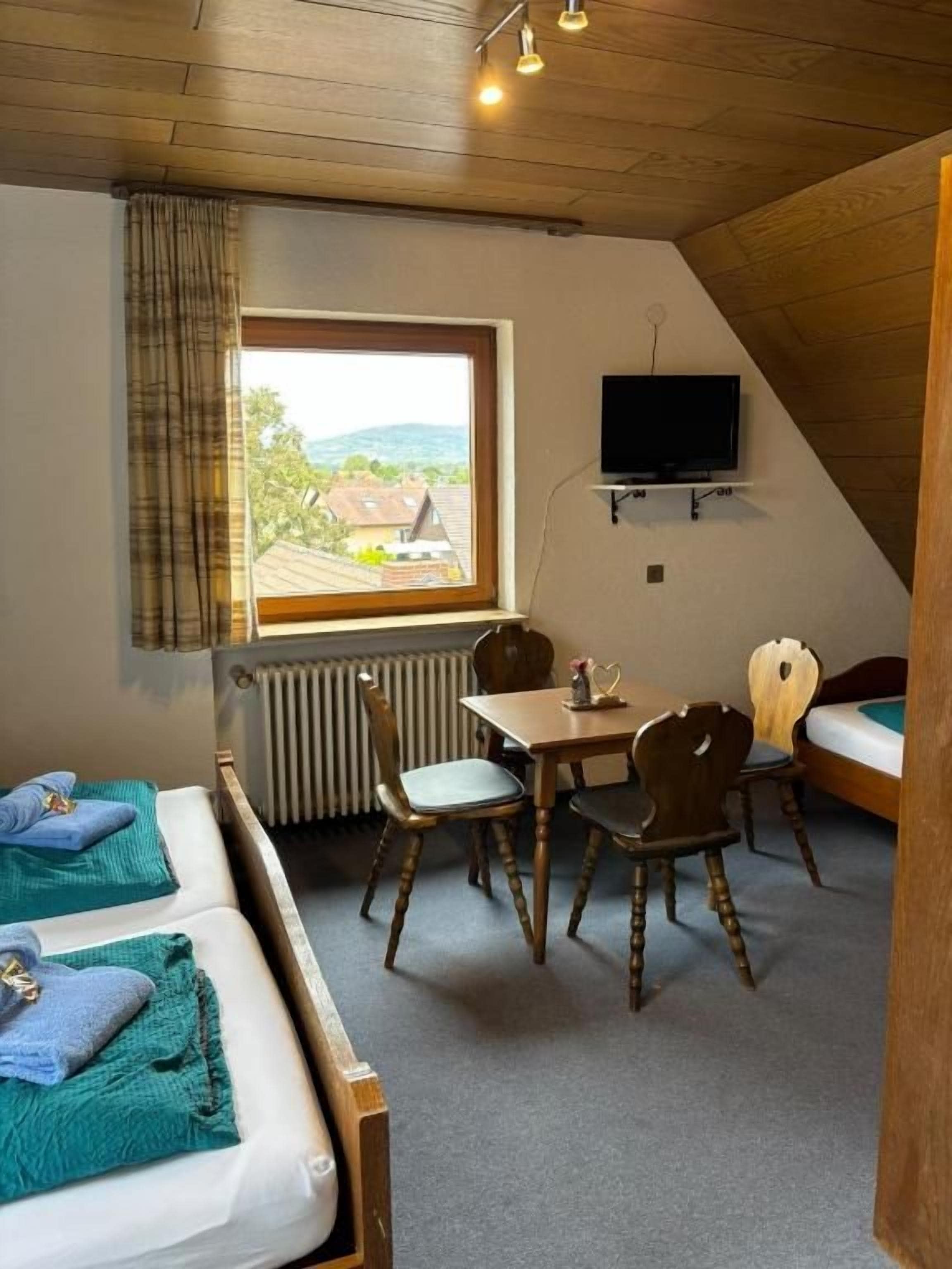 Une chambre avec deux lits, une table, des chaises, un téléviseur et une fenêtre donnant sur un beau paysage.