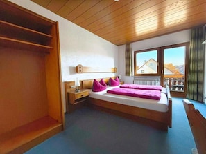 A bedroom with a bed, a nightstand, a wooden wardrobe, and a window with a view of buildings. - Gasthof Keller (Merdingen)