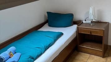 A single bed with a blue pillow and a white blanket, a wooden nightstand with a lamp, and a skylight above.