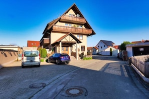 A two-story building with a balcony, parked cars, and a clear sky.