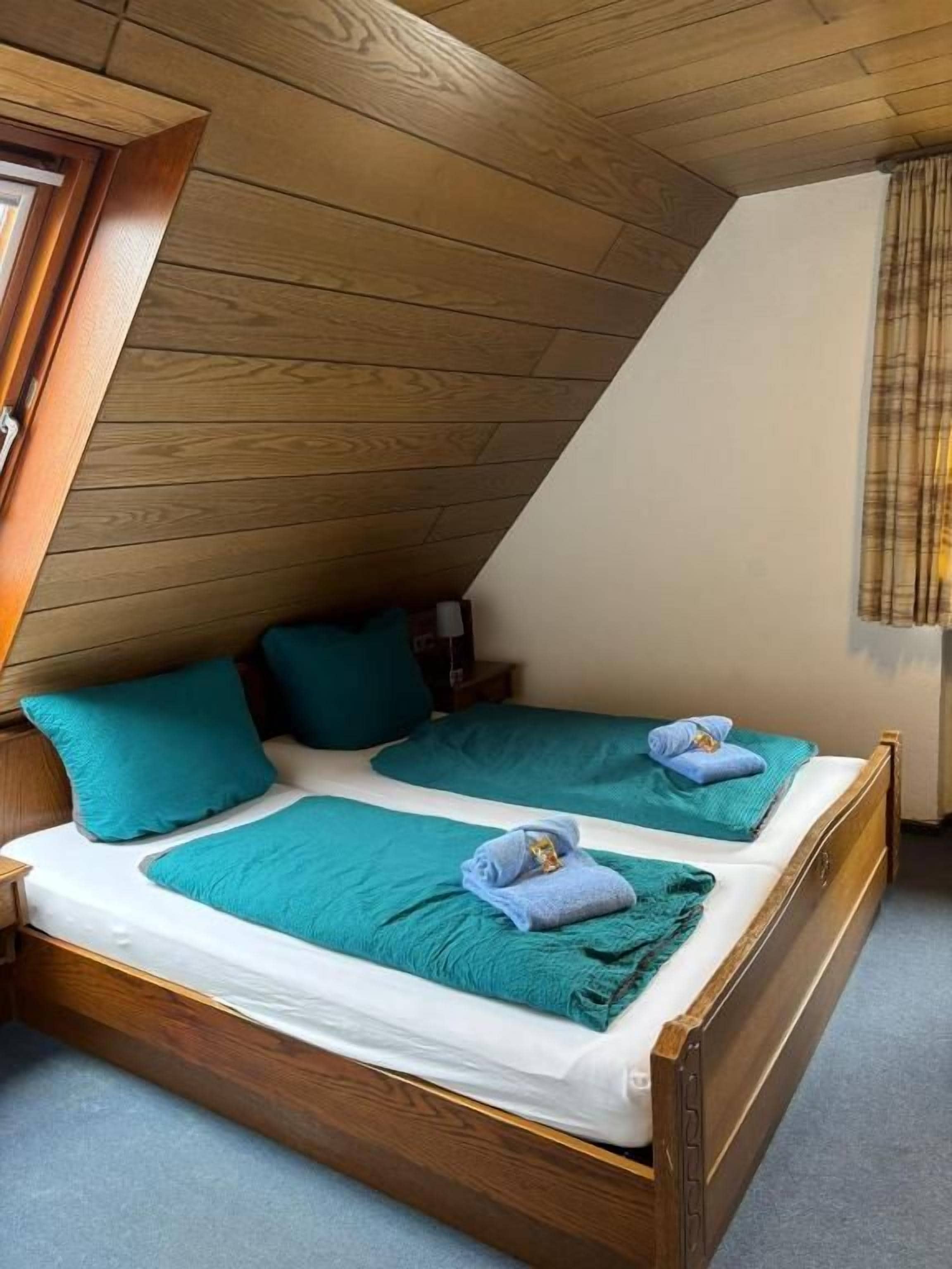 A room with a sloped ceiling, two beds with matching headboards, and a window with curtains.