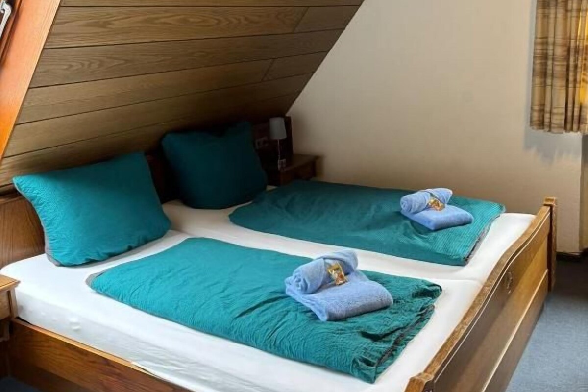A room with a sloped ceiling, two beds with matching headboards, and a window with curtains.