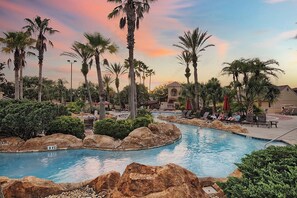 A pool area with palm trees, lounge chairs, and a building in the background. - Cozy Stay near Disney w/Pool, Lazy River & Resort (Davenport)