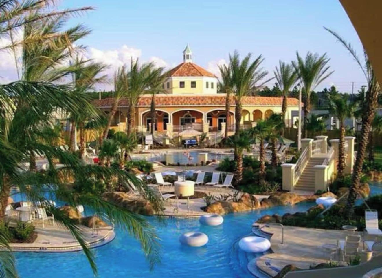 A resort with a swimming pool, palm trees, and a building with a dome roof.