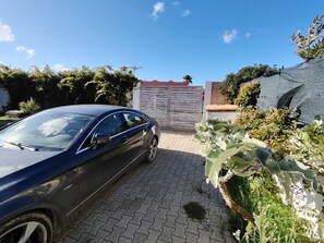 A car parked in a driveway with a gated entrance, a paved path, and various plants. - Villa Anemone: Relax by the Pool and the Sea (Sicilia)