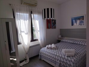A bedroom with a bed, a radiator, a window with curtains, a wall-mounted air conditioner, and a painting. - Villa Anemone: Relax by the Pool and the Sea (Sicilia)