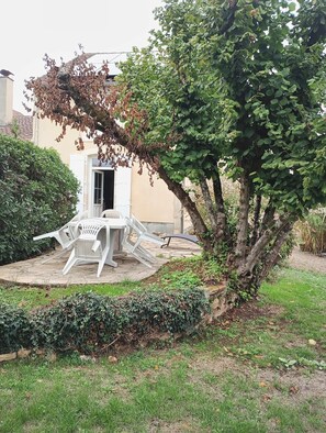 A patio with a table and chairs, a tree, and a building in the background. - Charm and tranquility near Futuroscope and Chauvigny (Bonnes)