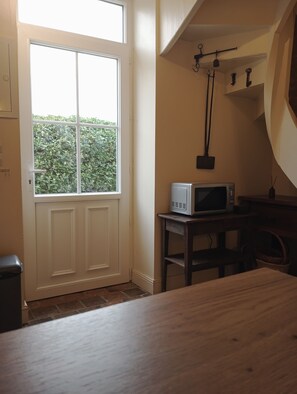 A room with a white door, a window with a view of greenery, a microwave on a small table, and a wooden table. - Charm and tranquility near Futuroscope and Chauvigny (Bonnes)