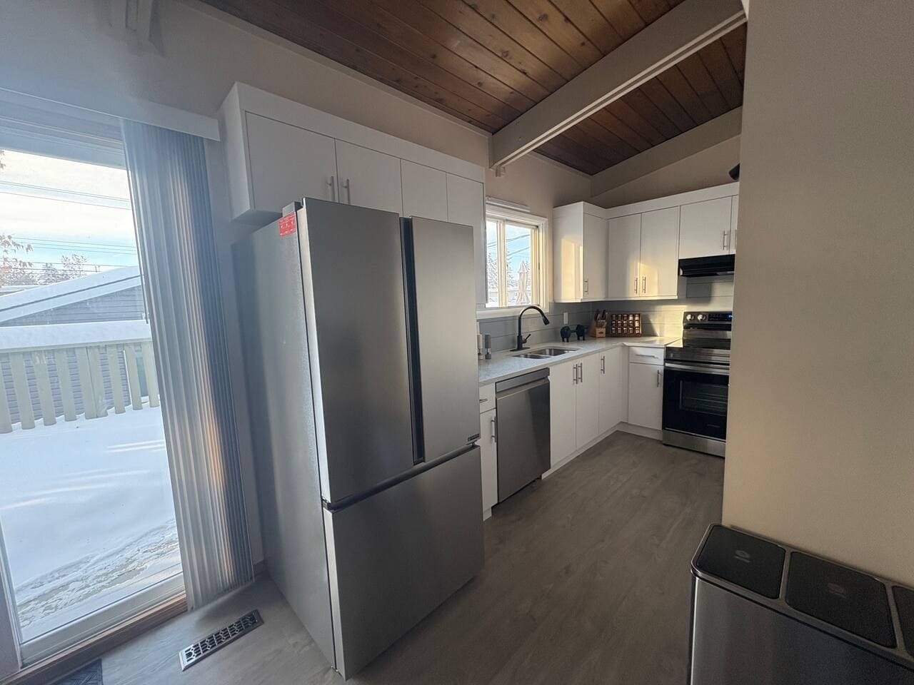 A modern kitchen with stainless steel appliances, white cabinetry, and a large window providing a view of the outdoors.