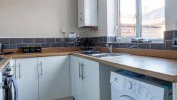 A compact kitchen with a washing machine, a window, and a tiled backsplash.
