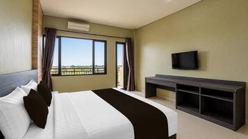 Una habitación de hotel con cama, escritorio, televisor y ventana con cortinas.