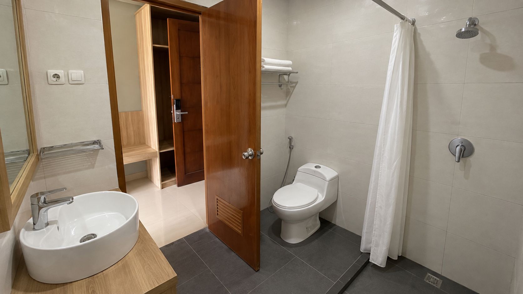A bathroom with a sink, toilet, shower, and a wooden door leading to a closet.