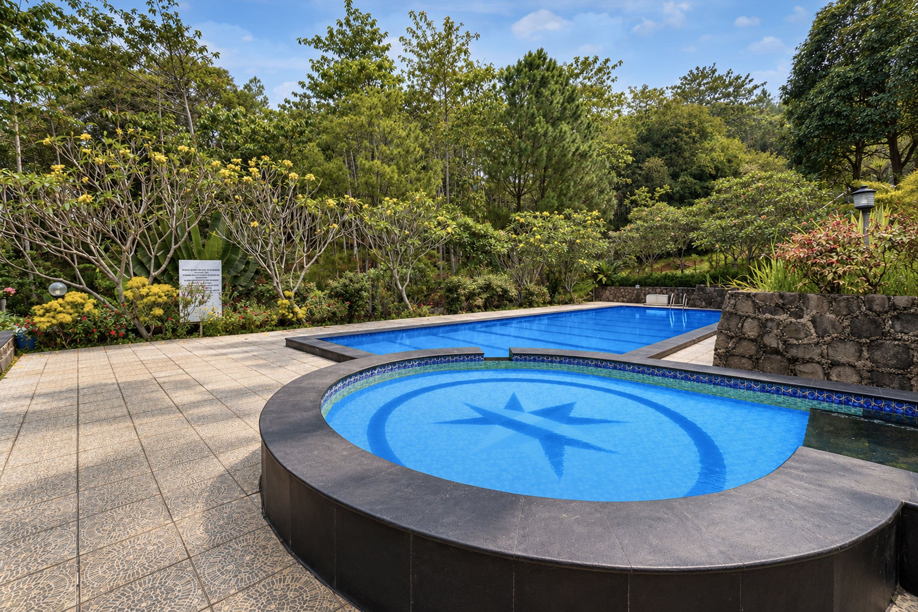 Una piscina con diseño de estrella, rodeada por un muro de piedra y abundante vegetación.
