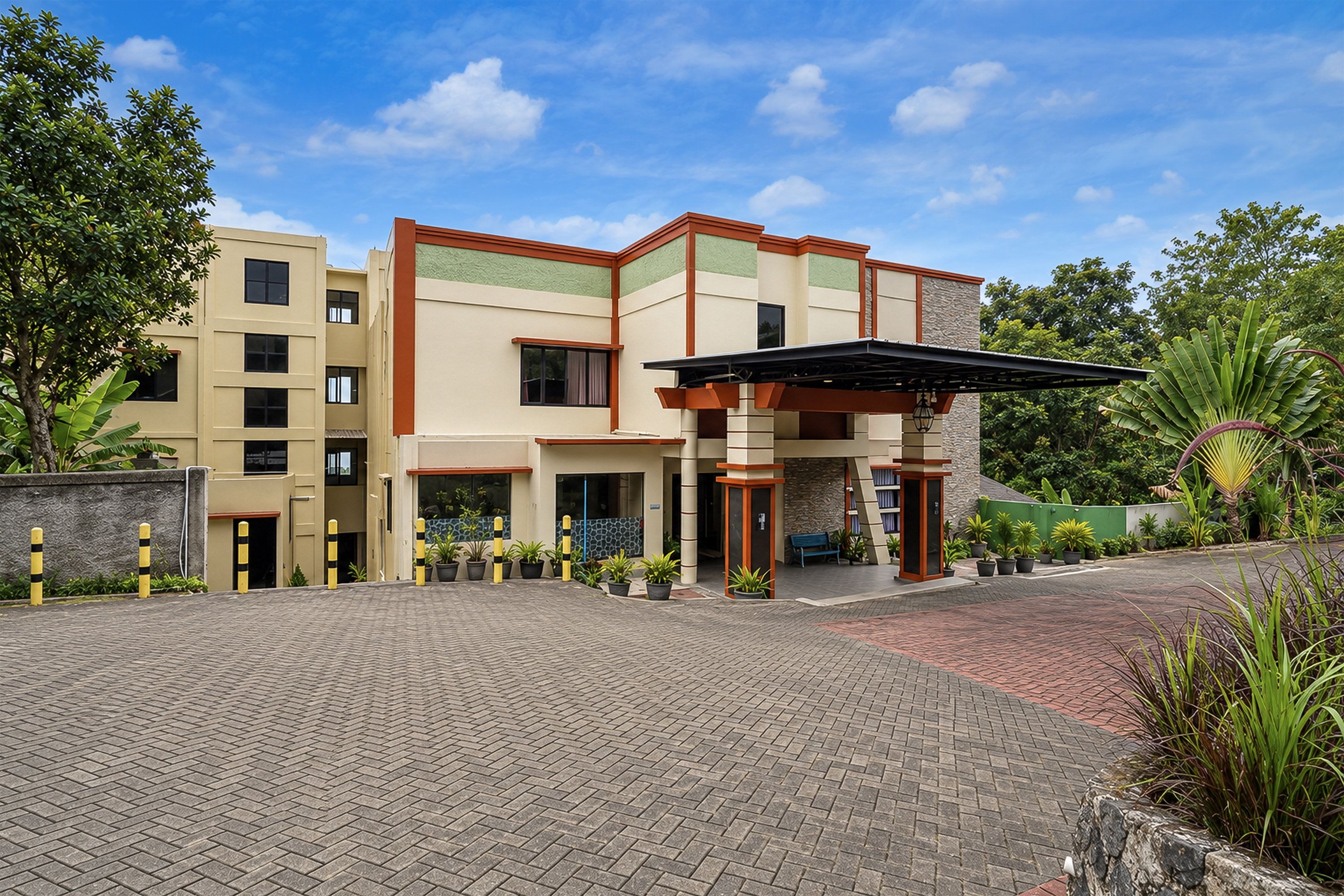 A modern hotel with a brick-paved entrance, multiple balconies, and a covered outdoor area.
