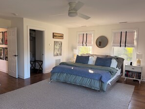 Un dormitorio con cama, mesitas de noche, ventilador de techo y una ventana con persianas.