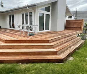 A modern outdoor deck with wooden steps leading to a seating area with a table and chairs. - Family home on large section near the river (Albert Town)
