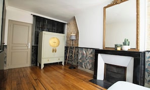 A room with a wooden floor, a white door, a white cabinet with a round mirror, a black and white patterned fireplace, and a large mirror on the wall. - CHARMING 2-BEDROOM MARAIS APARTMENT WITH LOCAL CHARACTER (Paris)