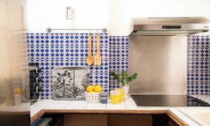 A kitchen with blue and white patterned tiles, a stainless steel range hood, and a black countertop. - CHARMING 2-BEDROOM MARAIS APARTMENT WITH LOCAL CHARACTER (Paris)