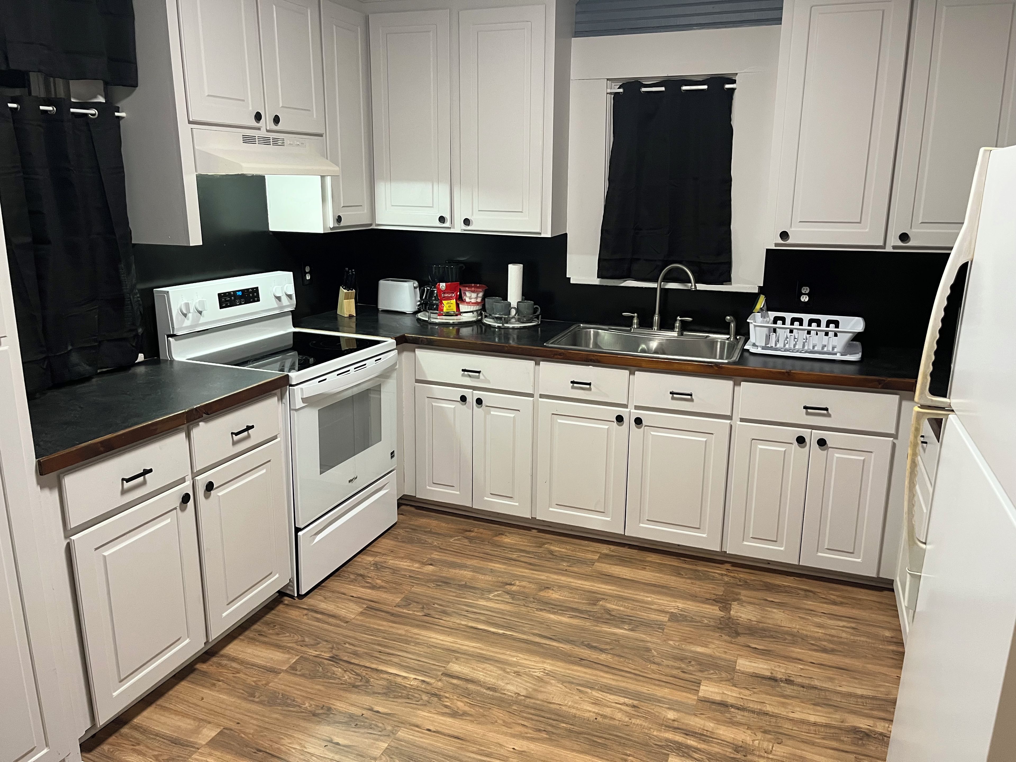 A kitchen with white cabinets, a black countertop, a stainless steel sink, and a white refrigerator.