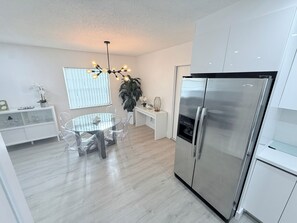 Eine moderne Küche mit einem Edelstahl-Kühlschrank, einem Esstisch mit Glasplatte und Stühlen sowie einer Pendelleuchte.