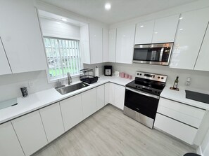 A modern kitchen with white cabinets, stainless steel appliances, a window with a view, and a black countertop.