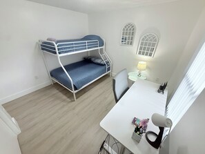 A bunk bed with a desk and chair, a lamp, and a window with blinds.