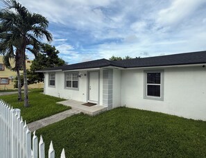A single-story house with a white exterior, a dark roof, and a small front porch.