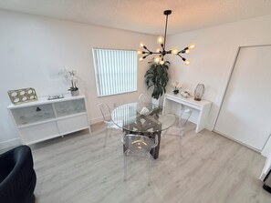 A modern dining area with a glass table and chairs, a white console, and a ceiling light fixture.