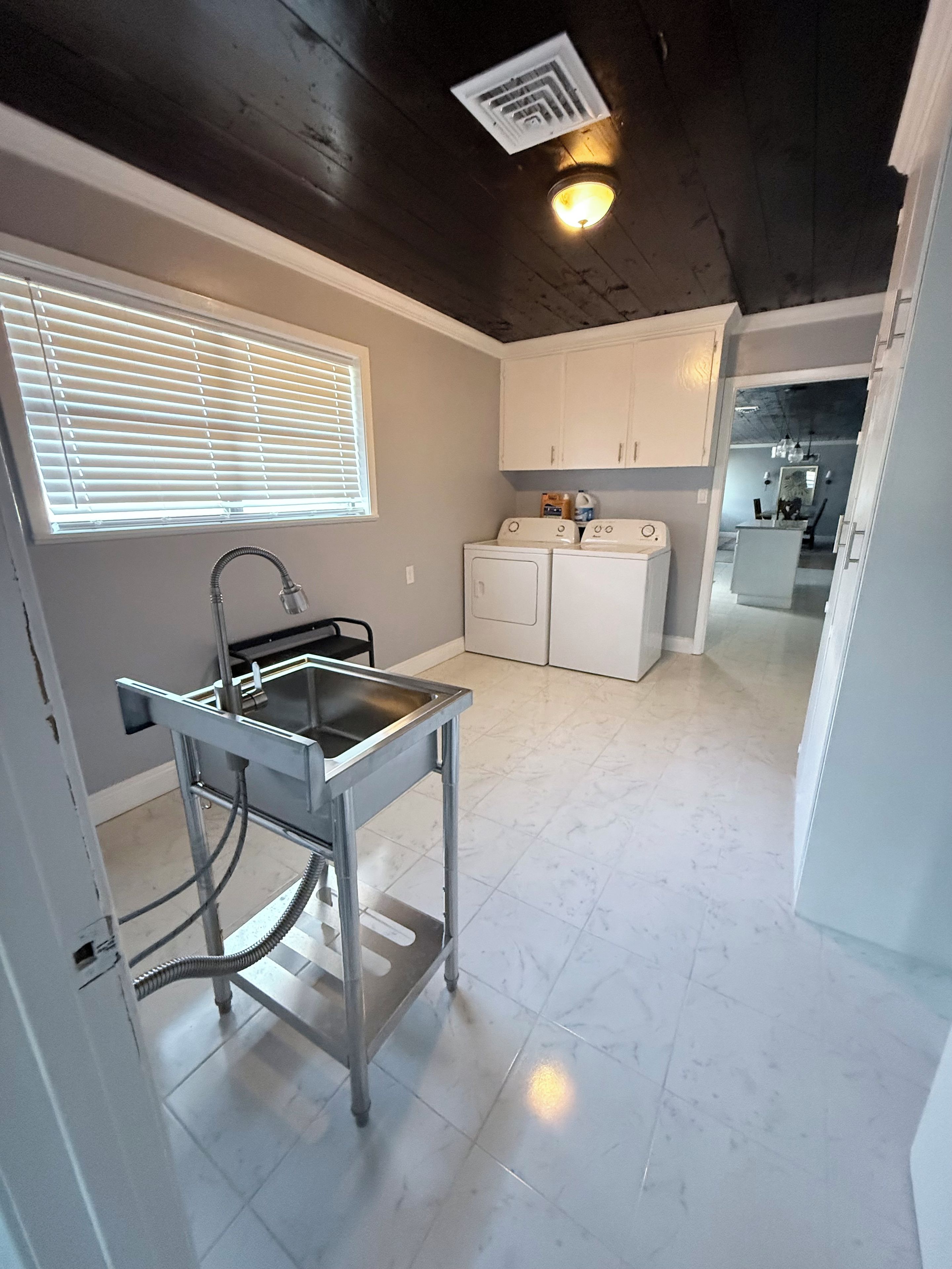 A laundry area with a washing machine and dryer, a sink with a hose, and a window with blinds.