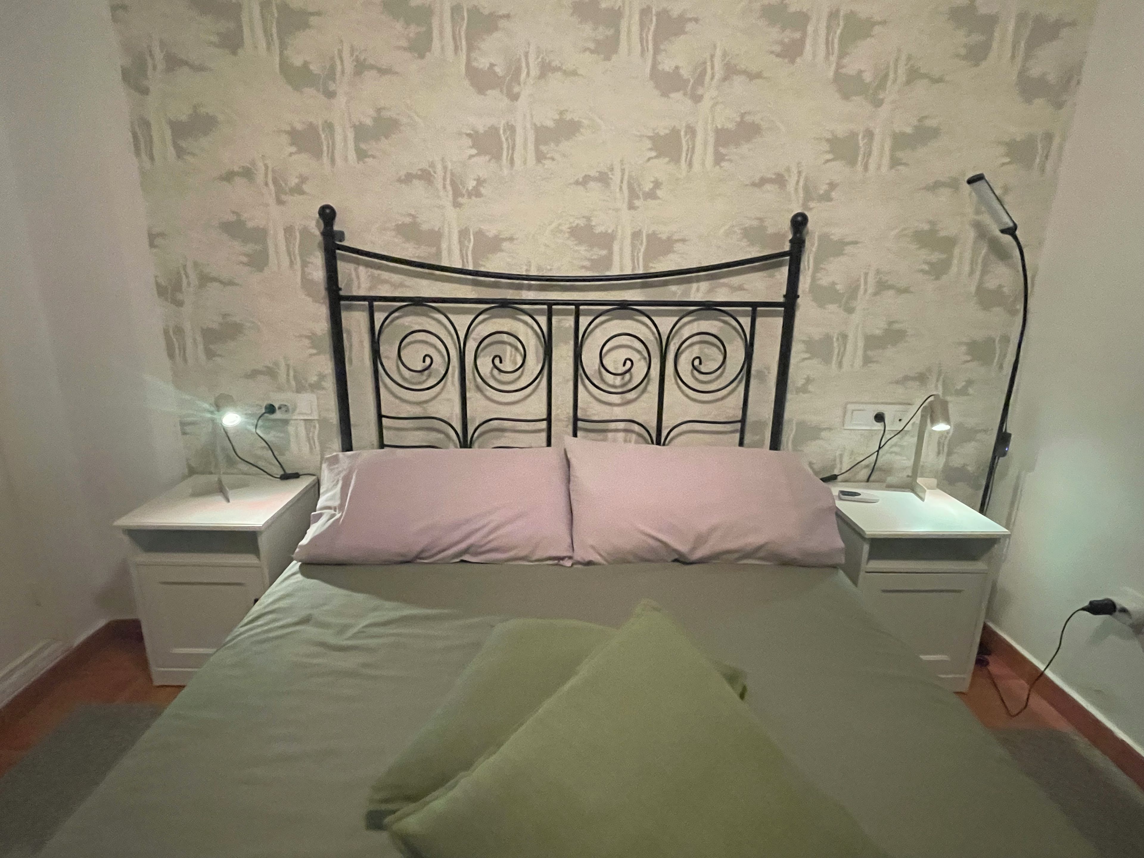 A bed with a metal headboard, two bedside tables with lamps, and a patterned wallpaper background.