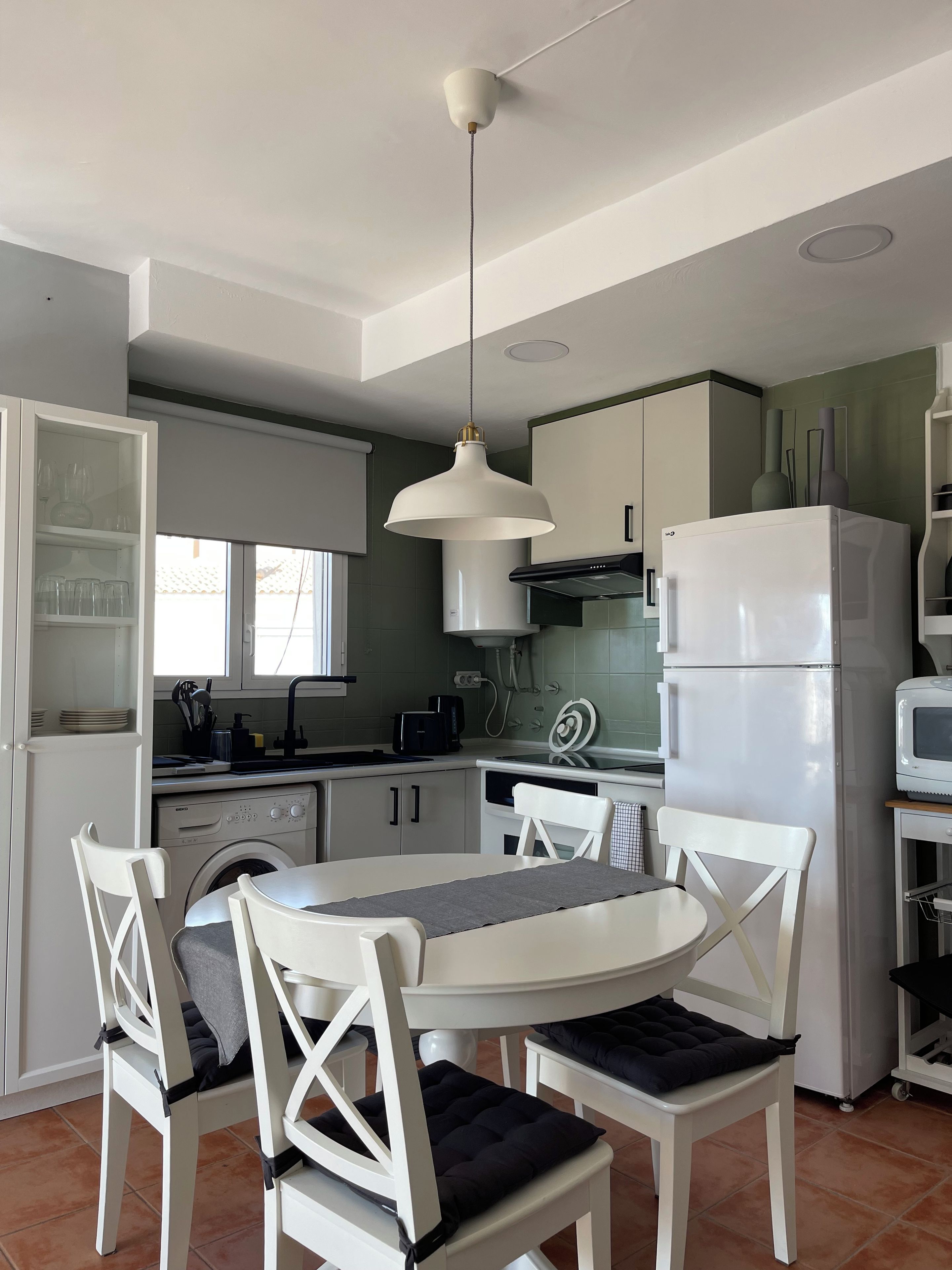 A kitchen with white cabinets, a white refrigerator, a microwave, and a dining table with chairs.