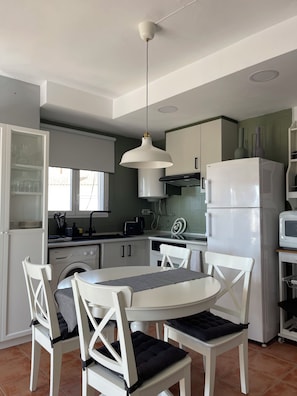 Una cocina con armarios blancos, un refrigerador blanco, un microondas y una mesa de comedor con sillas.