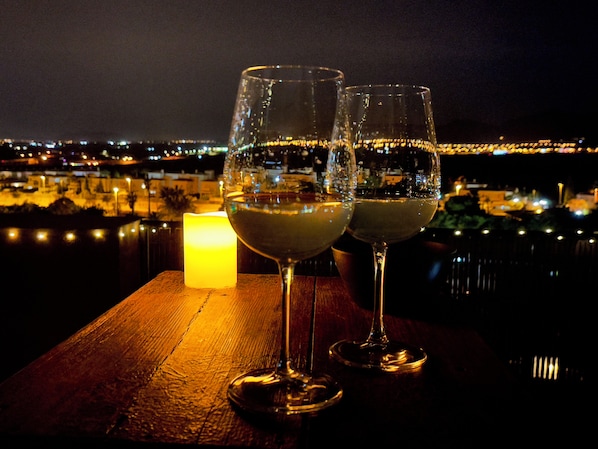 Deux verres de vin blanc sur une table en bois, avec une bougie allumée, donnant sur une vue nocturne de la ville.