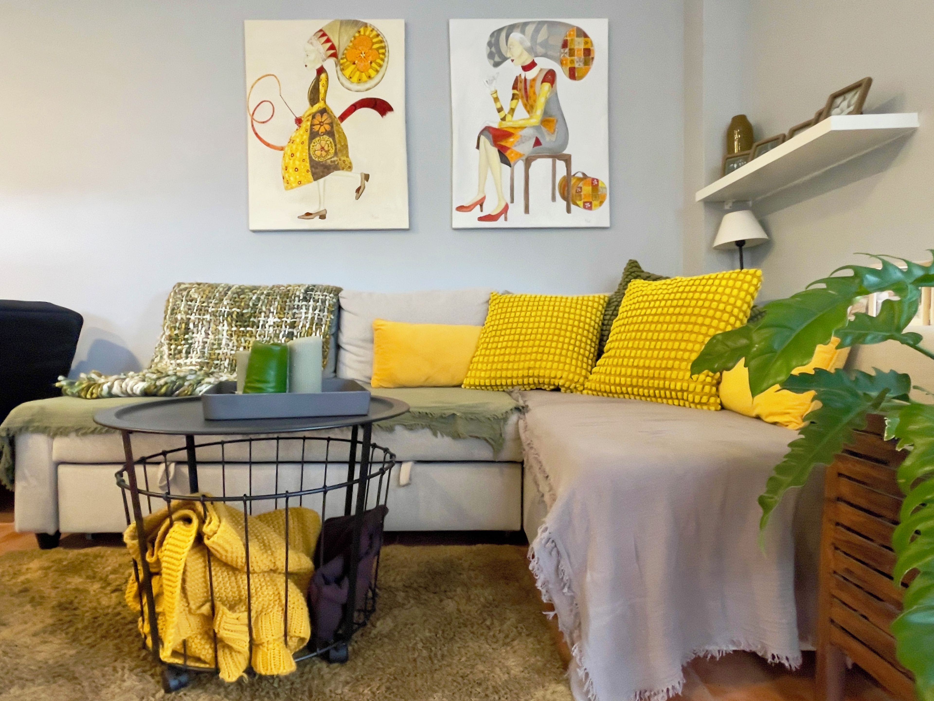 Un salón con sofá, cojines amarillos, una mesita de centro y una obra de arte en la pared.