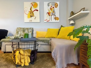 Un salon avec un canapé, des coussins jaunes, une table basse et des œuvres d’art accrochées au mur.