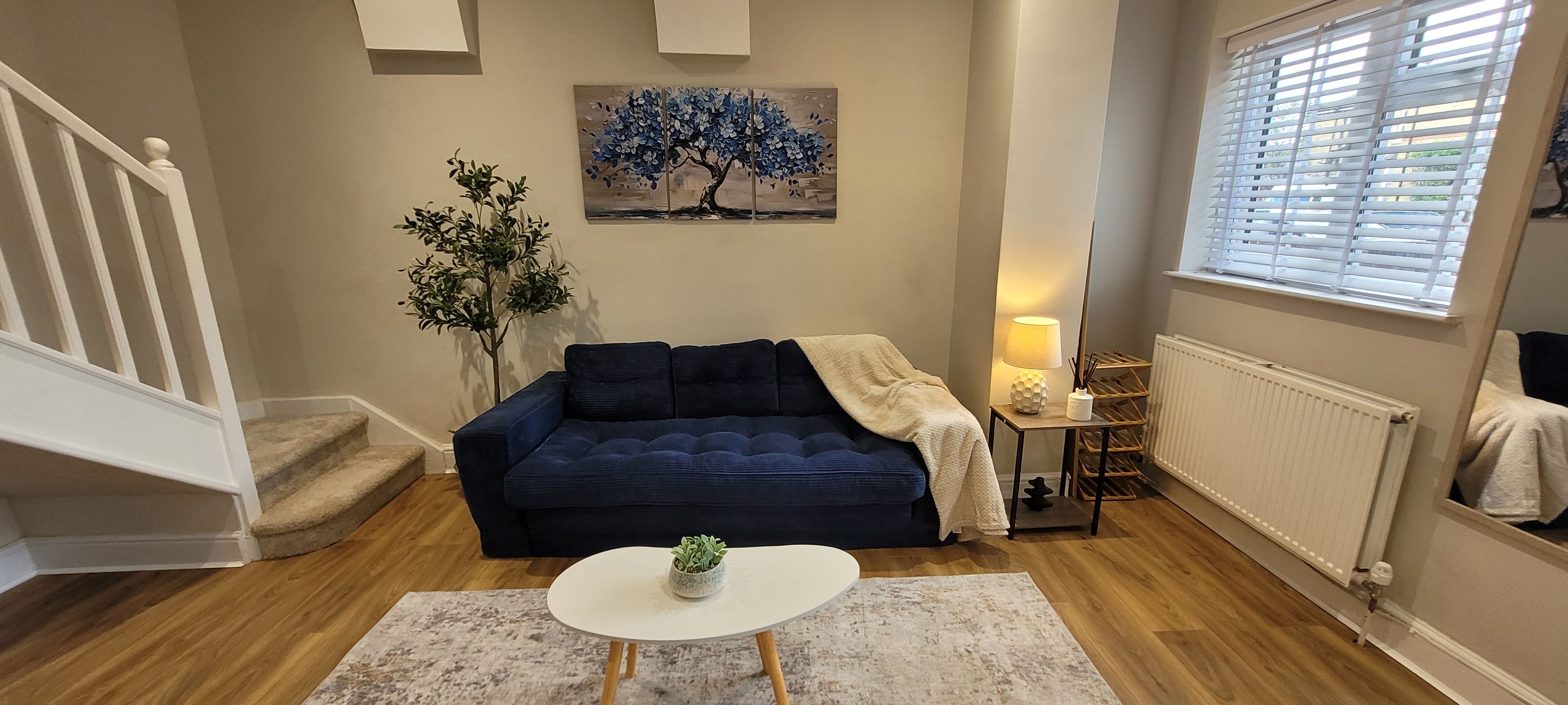A living room with a dark blue sofa, a white coffee table, a painting of a tree, and a radiator.