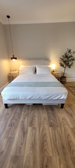 A bedroom with a large bed, wooden flooring, two bedside tables, a nightstand, a lamp, and a potted plant. - Unique and stylish, recently renovated house (Southampton)