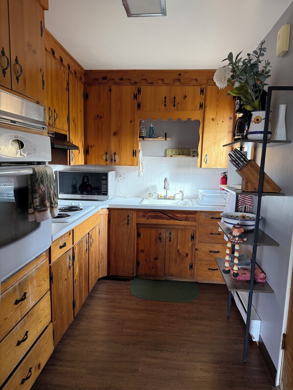Una cocina con armarios de madera, microondas, estufa, pileta y estante con utensilios de cocina.
