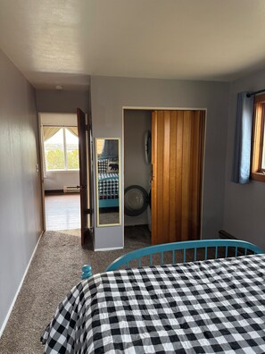 Un dormitorio con una colcha a cuadros, una puerta de madera, una lavadora y vistas a un balcón con una colcha a cuadros.