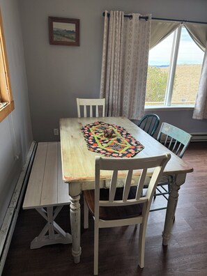 Un comedor con una mesa, sillas, un banco, una ventana con cortinas y un cuadro colgado en la pared.