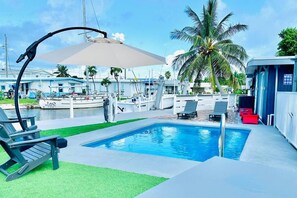 Ein Pool mit Liegestühlen und einem überdachten Bereich, umgeben von einer Marina mit Booten und Palmen.