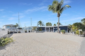 A building with a gravel driveway, a covered outdoor seating area, and palm trees. - Pipe Dream - Waterfront + Pool + 120' Dock (Marathon)