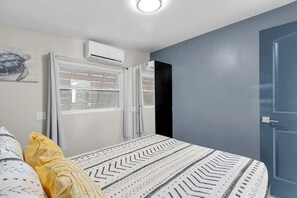 Ein Schlafzimmer mit Bett, einem Fenster mit Jalousien, einer Klimaanlage und einer Tür.