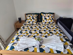 A bed with a geometric patterned bedspread, two pillows, a bedside table with a lamp, and a black headboard. - Azure Ti Briz (Les Trois-Îlets)