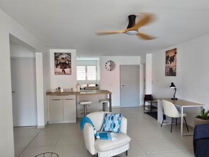 A modern kitchen with a central island, a dining area with a white table and chairs, a ceiling fan, and artwork on the walls. - Azure Ti Briz (Les Trois-Îlets)