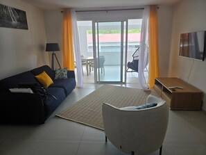 A modern living room with a sofa, a chair, a TV, and a balcony with yellow curtains. - Azure Ti Briz (Les Trois-Îlets)