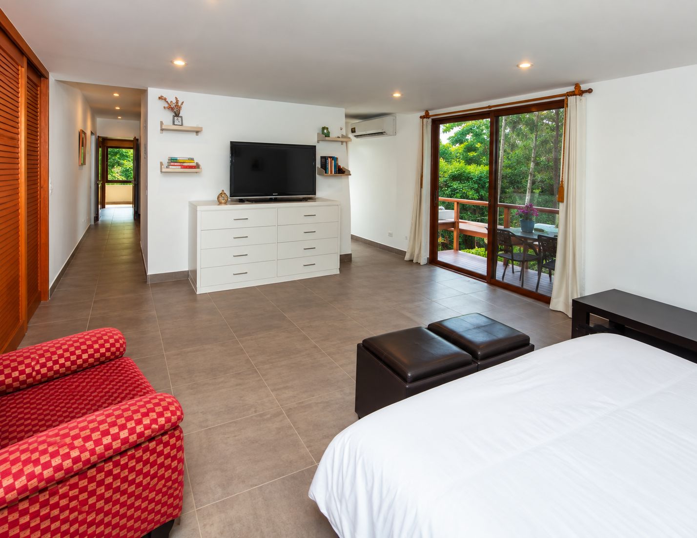 A bedroom with a bed, a TV, a dresser, and a balcony with a table and chairs.