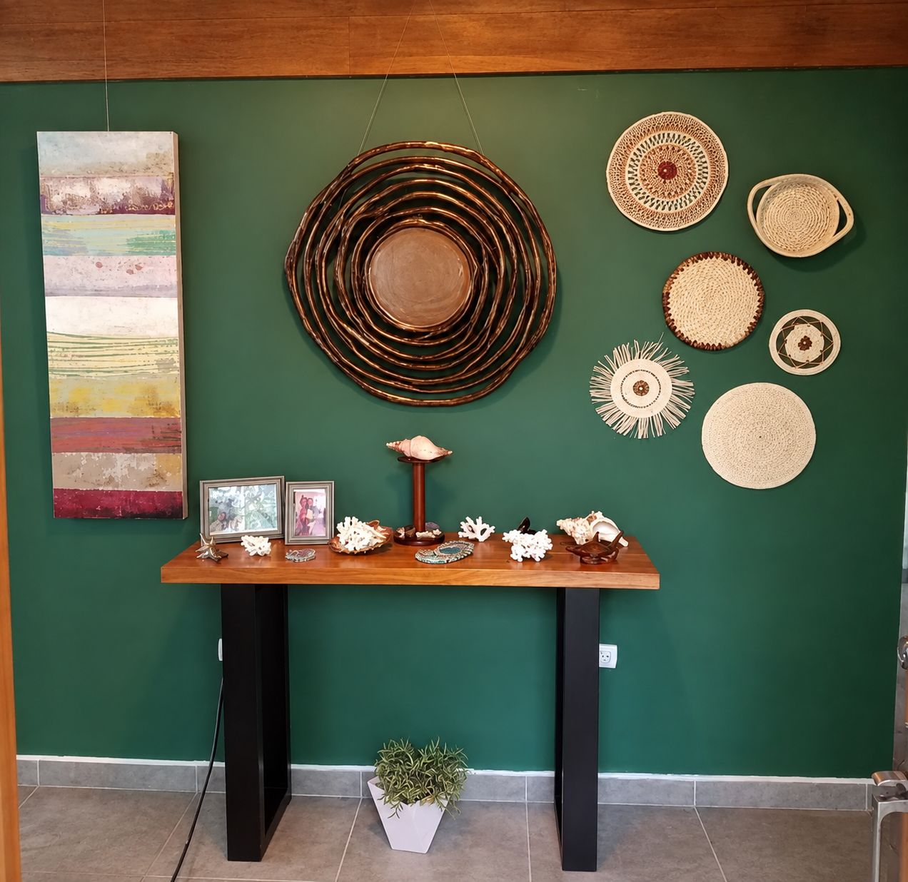 A room with a green wall, a wooden table with decorative items, and a hanging circular object.