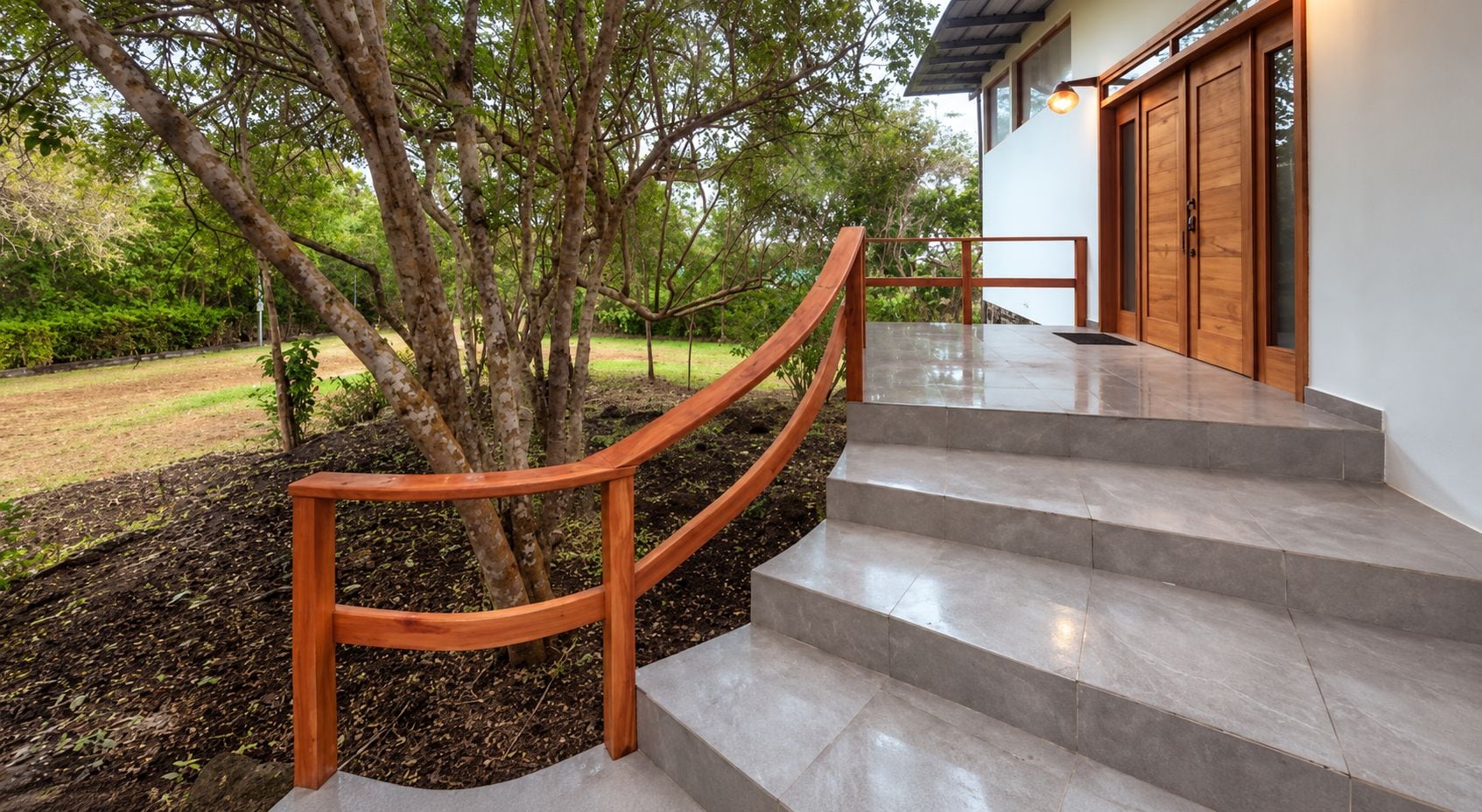 A staircase with a wooden handrail leading to a building with large wooden doors.