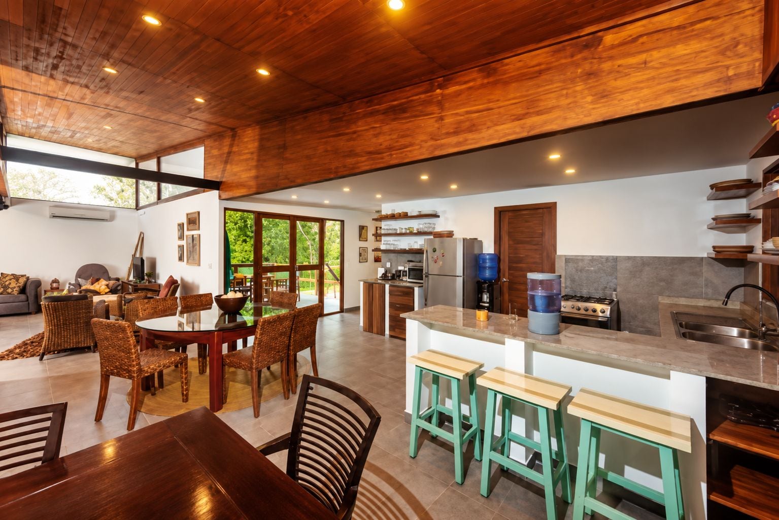 A modern kitchen with a central island, built-in appliances, and a dining area with wicker chairs.